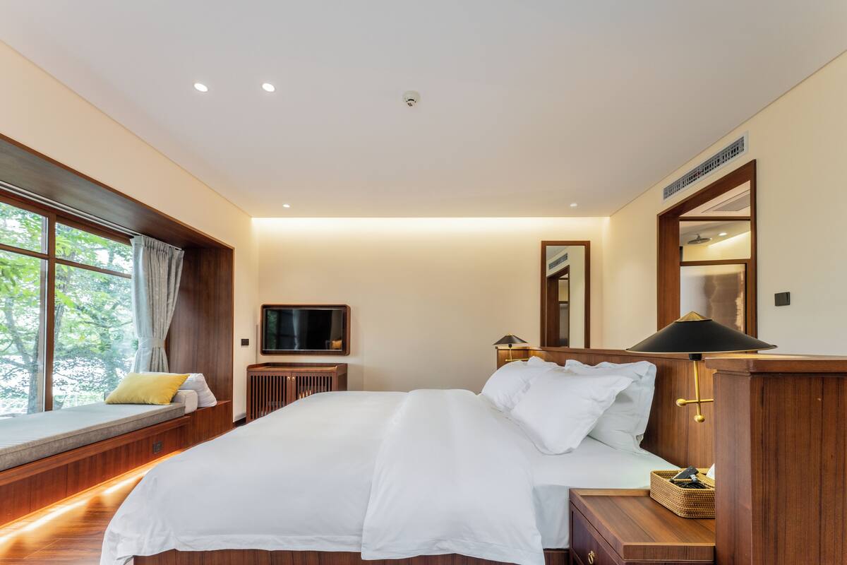 Ein Schlafzimmer mit einem großen Bett, einem Fernseher, einer Nachttischlampe und einem Fenster mit Vorhängen.