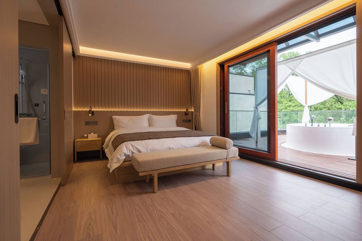 Ein modernes Schlafzimmer mit einem großen Bett, Nachttischen, einer Bank und einer Schiebetür zu einem Außenbereich.