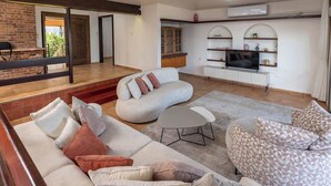 A modern living room with a sofa, armchair, and ottoman, a TV, and a fireplace.