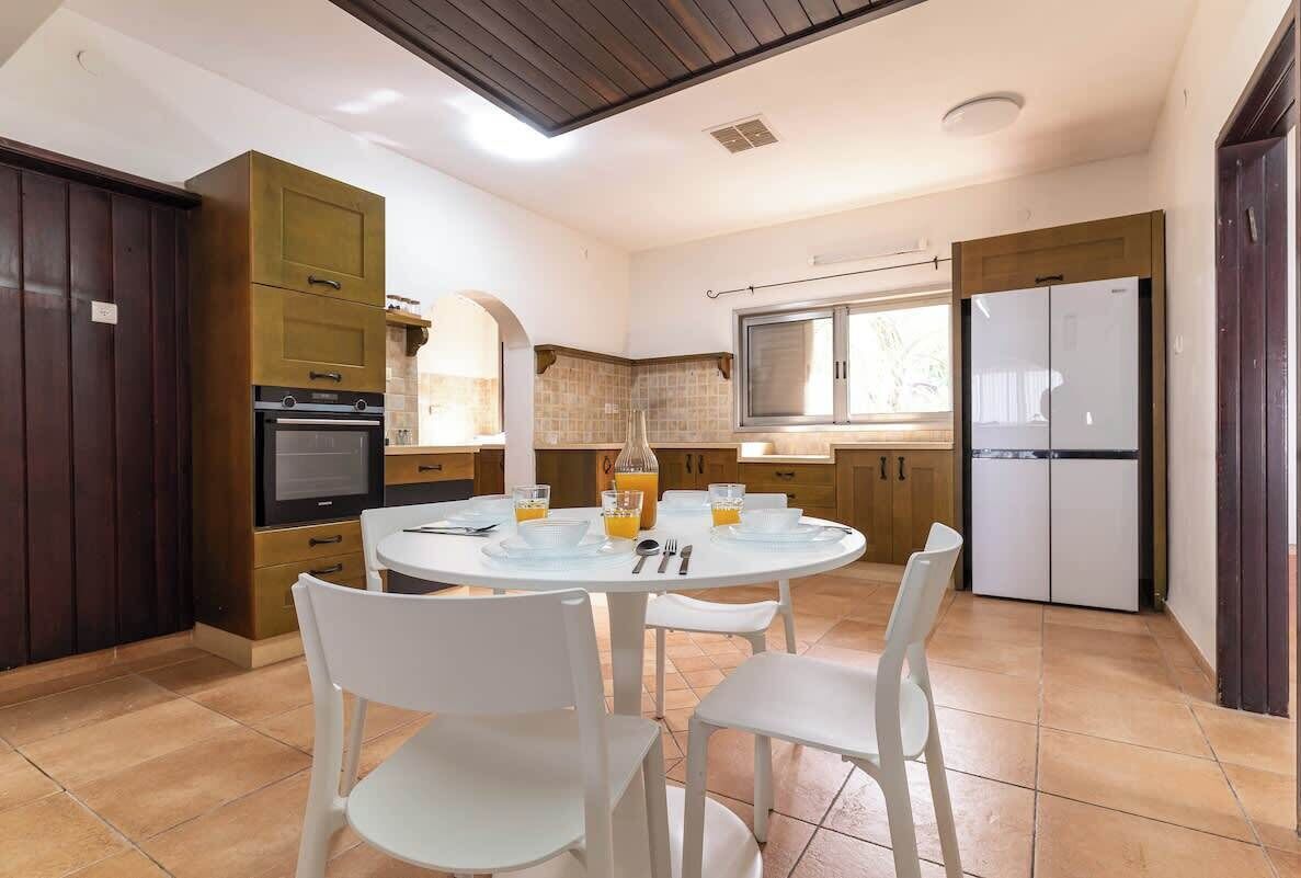 A modern kitchen with a dining table set for four, equipped with a refrigerator, oven, and microwave.