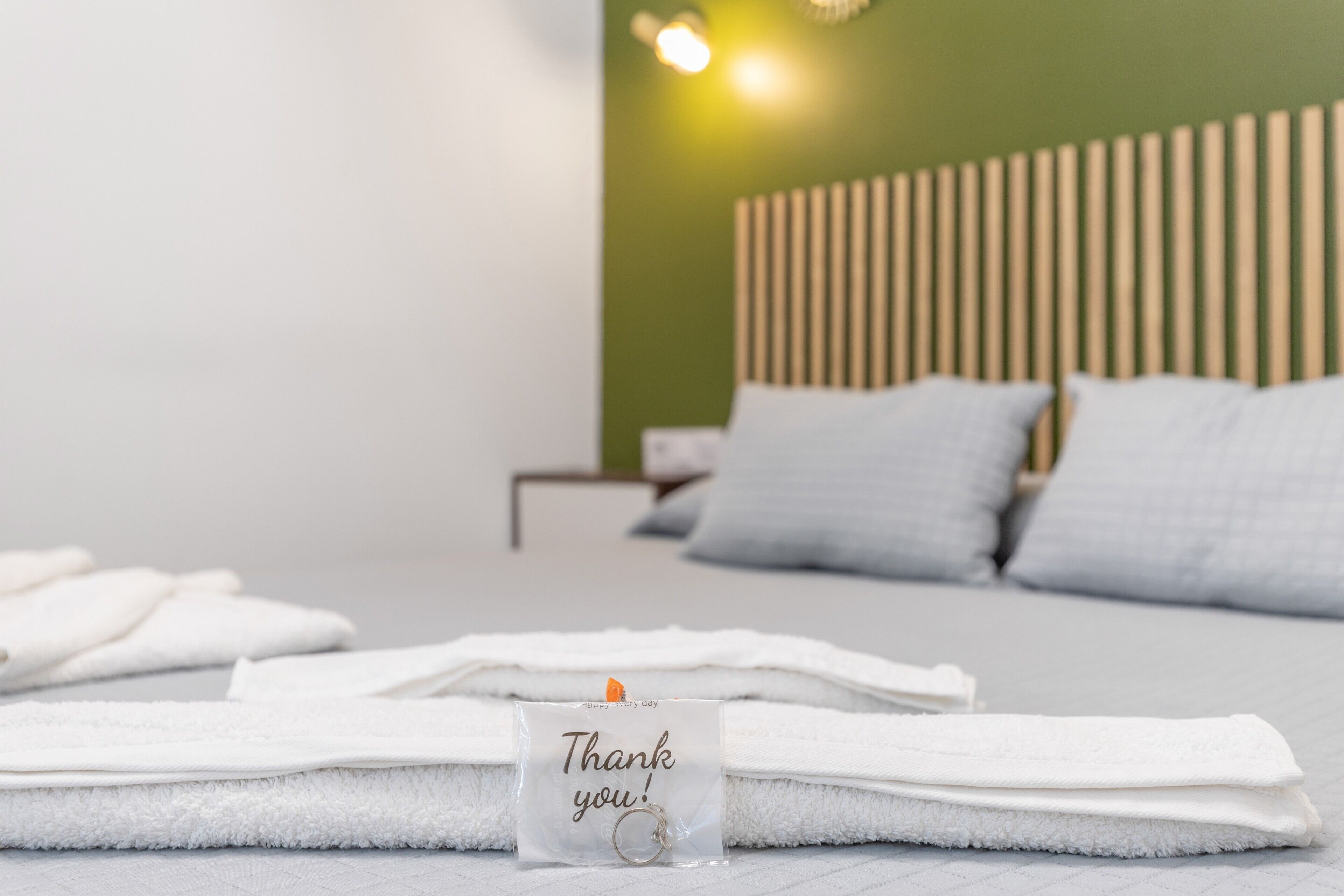 Una cama impecable con sábanas blancas, una tarjeta de agradecimiento y un cabecero de madera en una habitación moderna.
