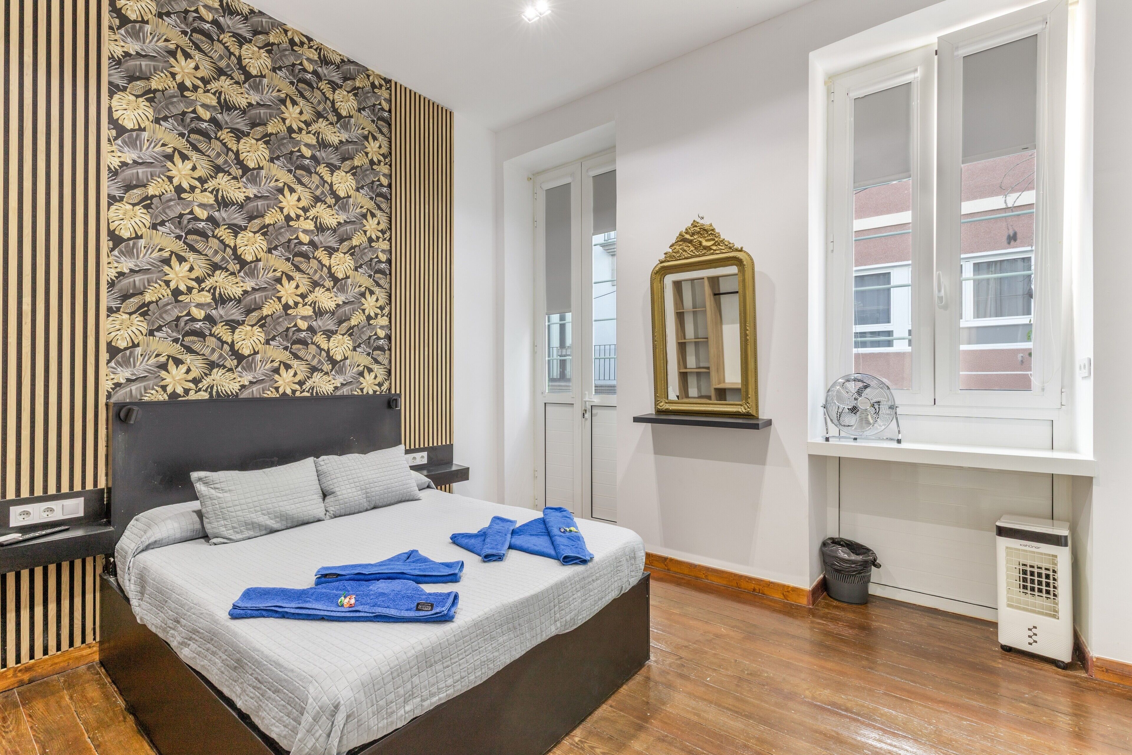 A bedroom with a bed, a wall with a leaf pattern, a mirror, a window, and a heater.