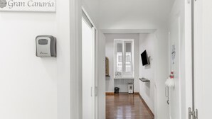 A hallway with a wooden floor, white walls, a door with a sign reading 'Gran Canaria,' a wall-mounted device, and a small trash bin. -  'Gran Canaria' with Balcony and Wi-Fi (Las Palmas de Gran Canaria)