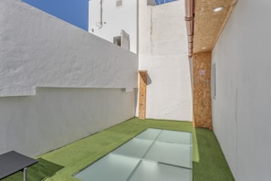 Un patio estrecho con piso de vidrio, paredes blancas y una puerta de madera.
