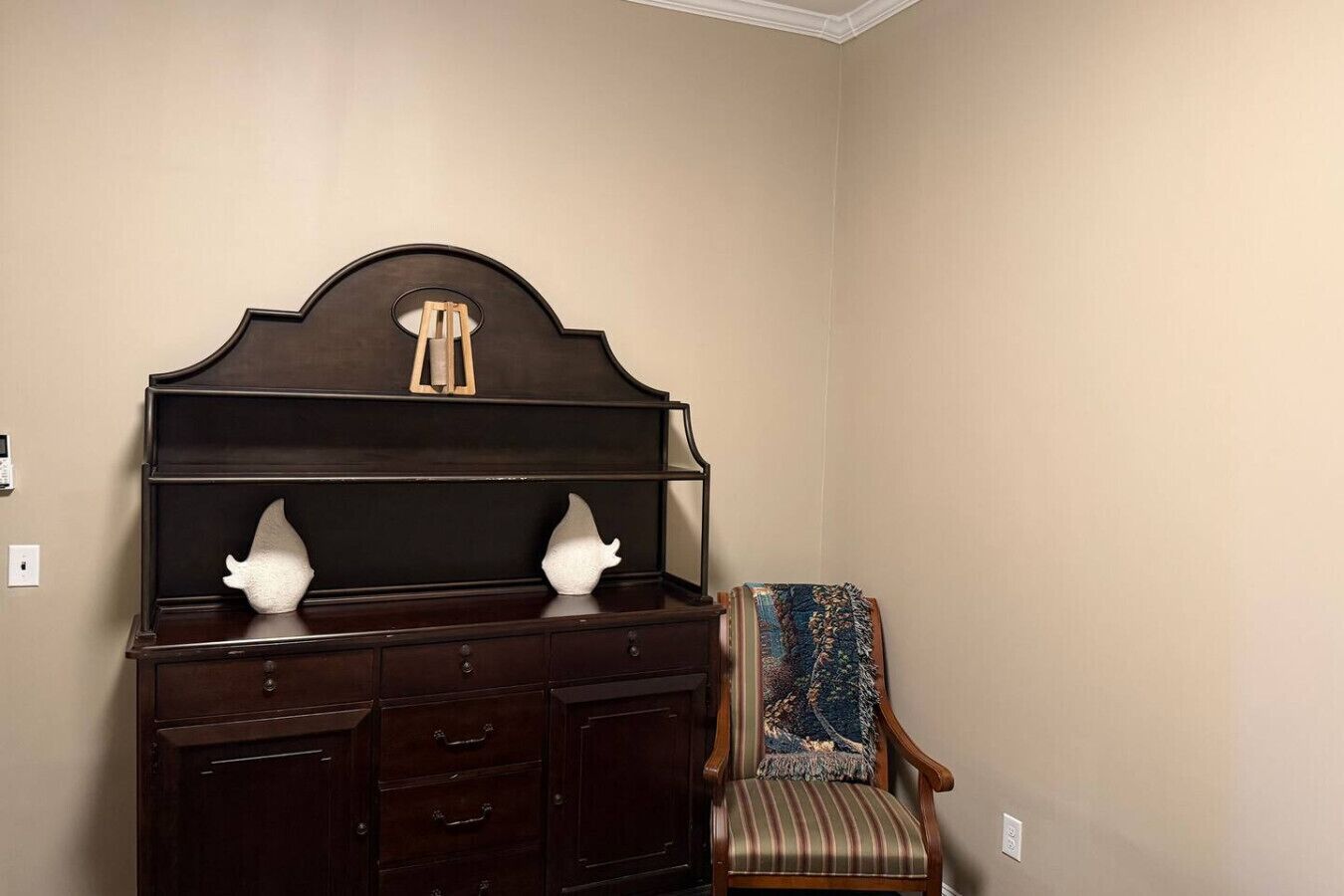 Een donker houten dressoir met twee decoratieve vazen, een stoel met een gestreept kussen, en een effen muur.
