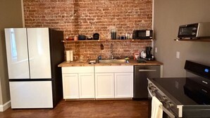 A kitchen with a brick wall, white cabinets, a refrigerator, a microwave, and a stove.