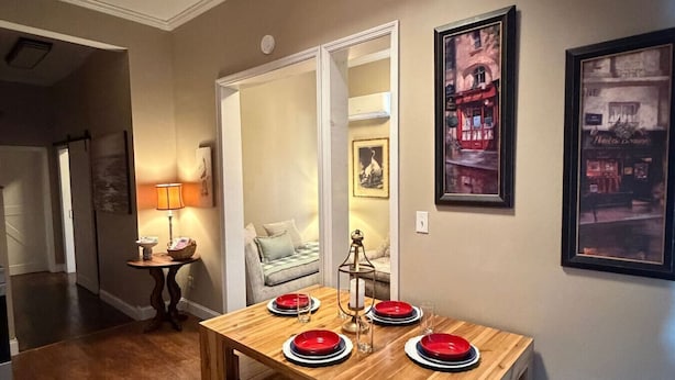 A dining area with a wooden table set for four, a lamp, and framed artwork on the walls.