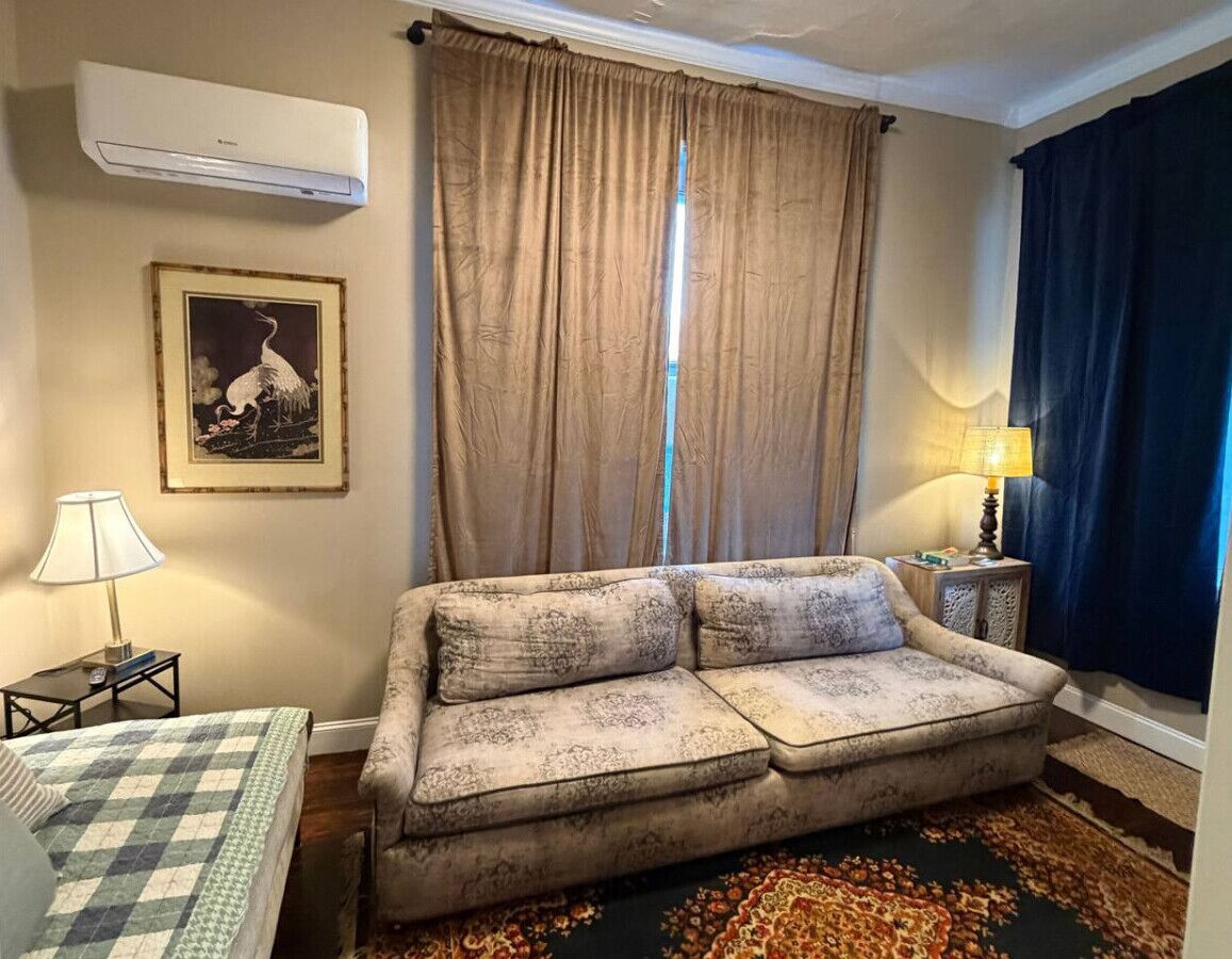 A living room with a sofa, a lamp, a framed picture, and a window with curtains.