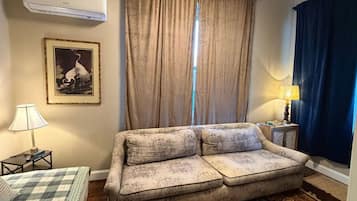 A living room with a sofa, a lamp, a framed picture, and a window with curtains.