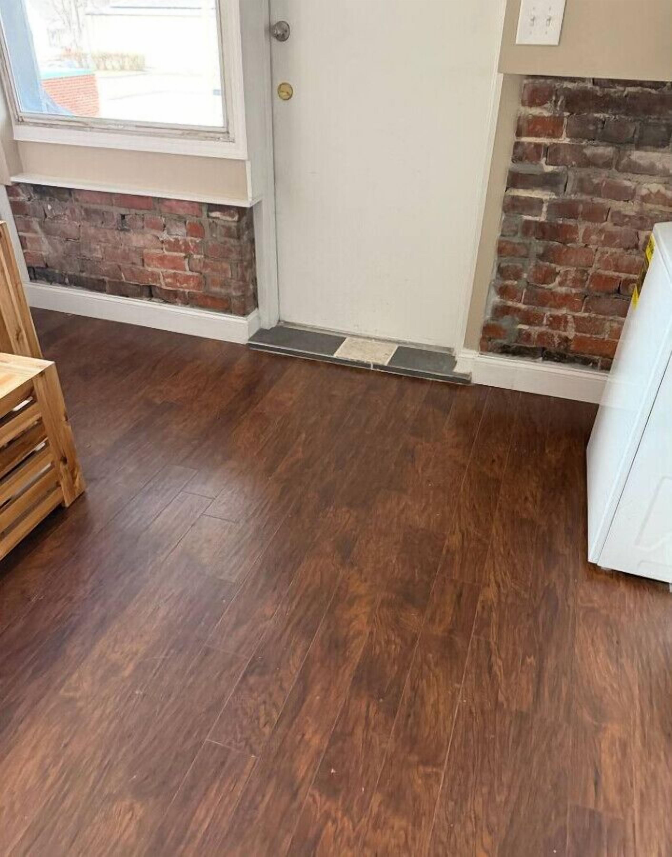 A room with a wooden floor, a door, a brick wall, and a window.