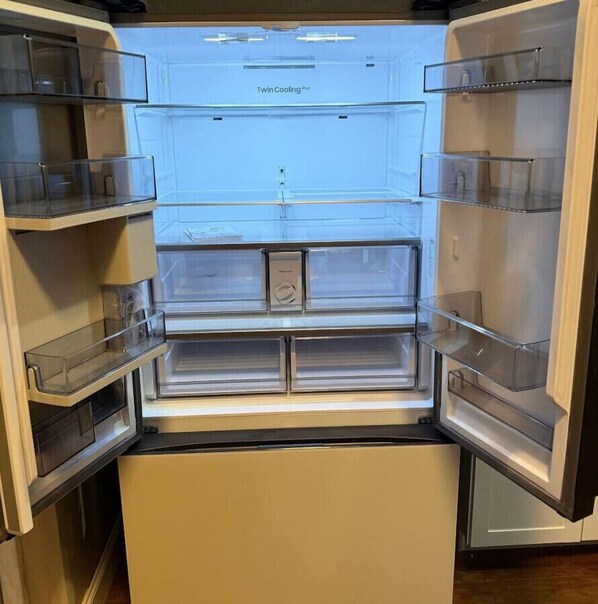 Un refrigerador abierto con múltiples estantes traslúcidos y un dispensador de hielo central.