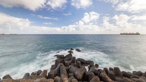 A coastal scene with waves crashing against a breakwater, a ship in the distance, and a clear sky. - Tenerife Room in Las Palmas de Gran Canaria (Las Palmas de Gran Canaria)