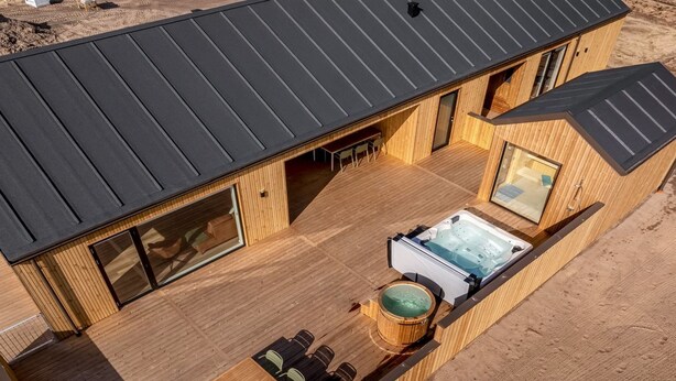 Una cabaña de madera con jacuzzi, mobiliario de exterior y un ventanal grande.