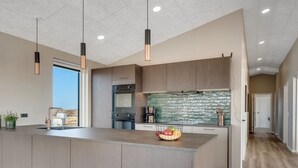 Una cocina moderna con una isla grande, electrodomésticos integrados e iluminación colgante.