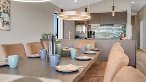 Un comedor moderno con una mesa larga, sillas acolchadas e iluminación colgante.