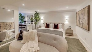 Una camera da letto moderna con un divano ad arco, un letto grande con molti cuscini, un comodino e uno specchio.