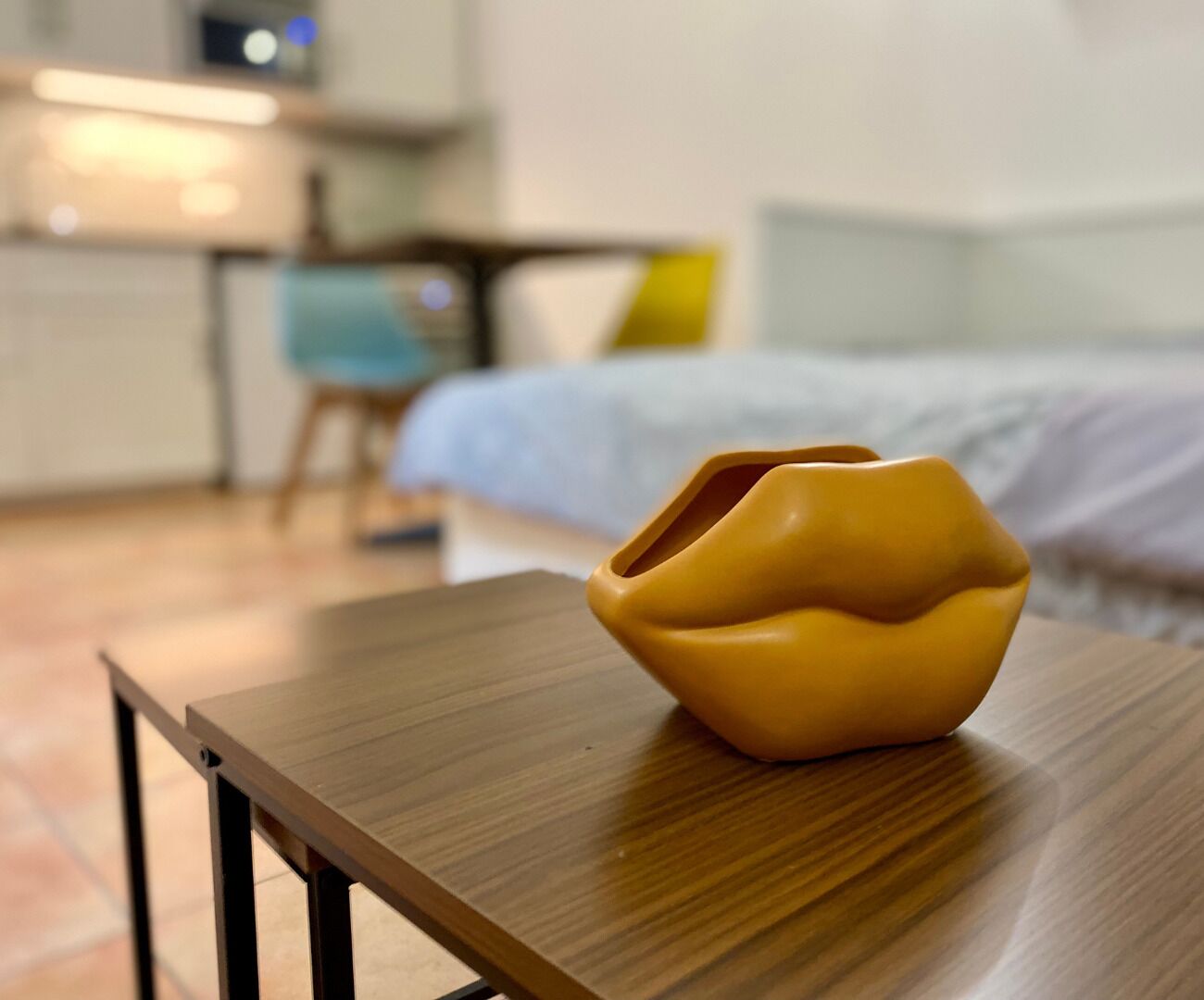 A yellow vase on a wooden table in a hotel room.