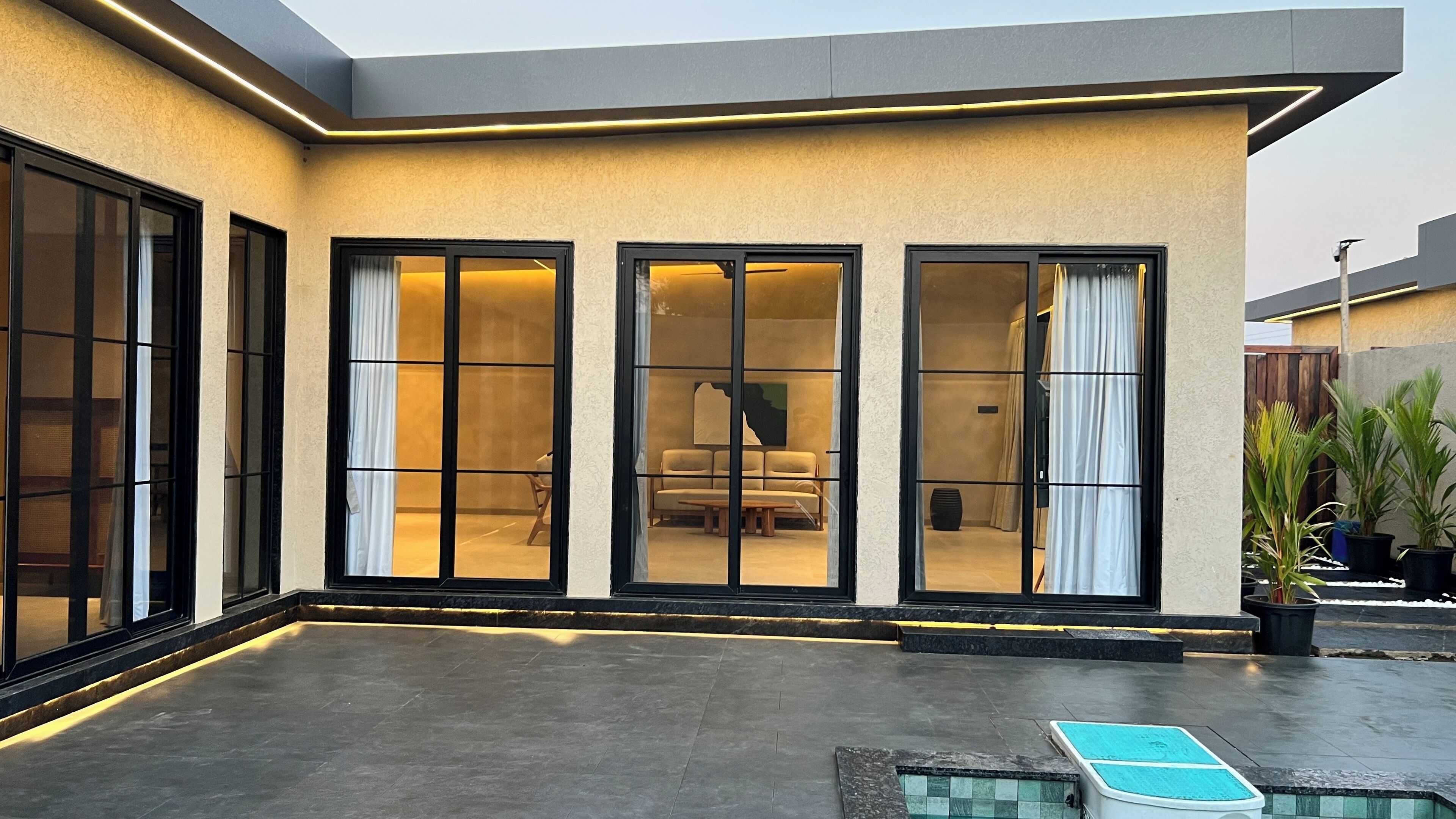 Un edificio moderno con grandes puertas correderas de vidrio, un área de piscina y plantas en macetas.