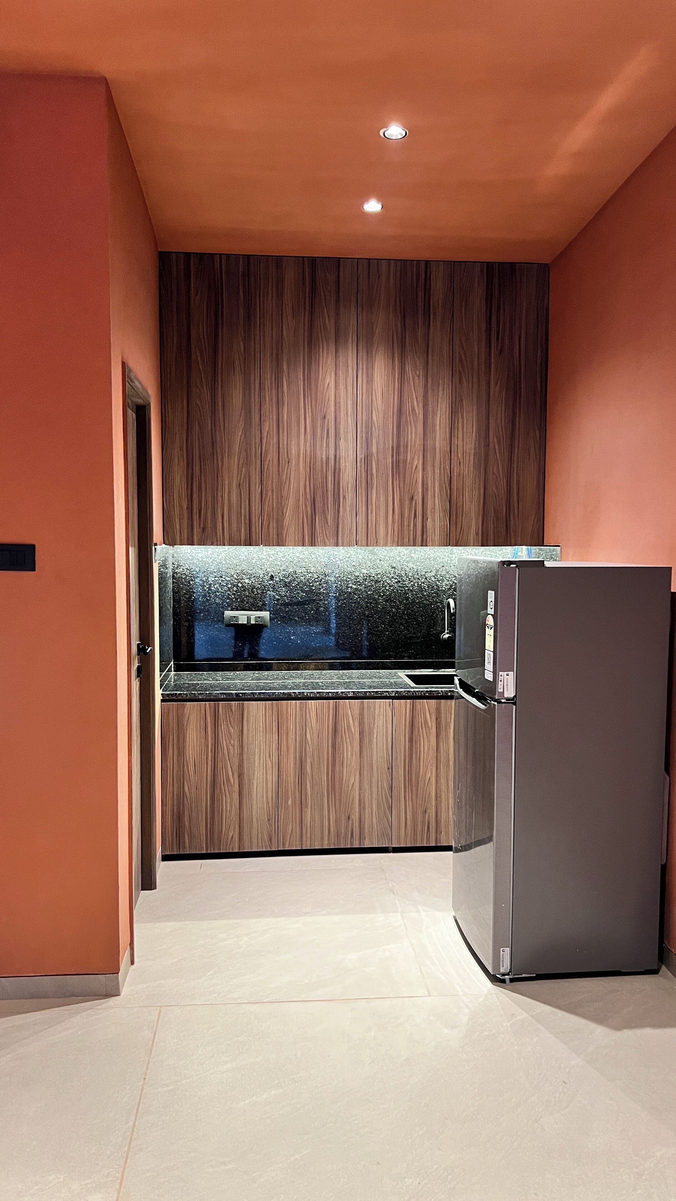 A modern kitchen with a wooden accent wall, a stainless steel refrigerator, and a built-in oven.