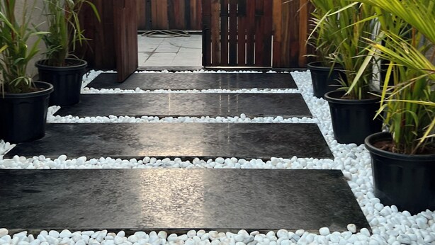 Un sendero conduce a una puerta de madera, bordeado por macetas con plantas y guijarros blancos.
