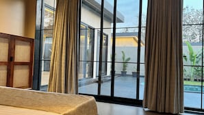 Una habitación con ventanas amplias, una cama y vista a un patio con plantas en macetas.