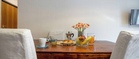 Una mesa de desayuno con bollos, fruta y una cafetera.