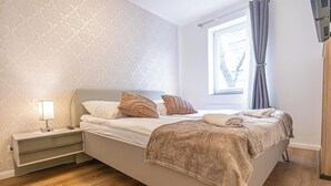 Siististi pedattu sänky, jossa on beigenvärinen peitto, yöpöytävalaisin ja kuviollinen seinä.