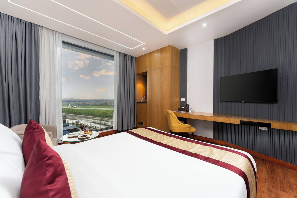 Une chambre d’hôtel avec un grand lit, un bureau, une chaise, une télévision et une vue sur un paysage.