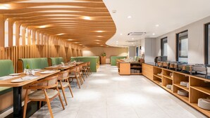 Egy modern étterem, melynek a falait fa borítás fedi, zöld színű, párnázott ülései vannak, és egy büféasztal is található benne.