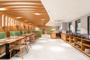 A modern restaurant with wooden panel walls, green cushioned seating, and a buffet area.