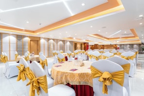 A banquet hall with round tables, white chairs with gold sashes, and a modern ceiling design. - Lords  CBC Plaza  Chitwan (Bharatpur)