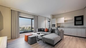 Un salon moderne avec un canapé d’angle gris, une petite table basse et une vue sur la ville grâce à de grandes fenêtres.