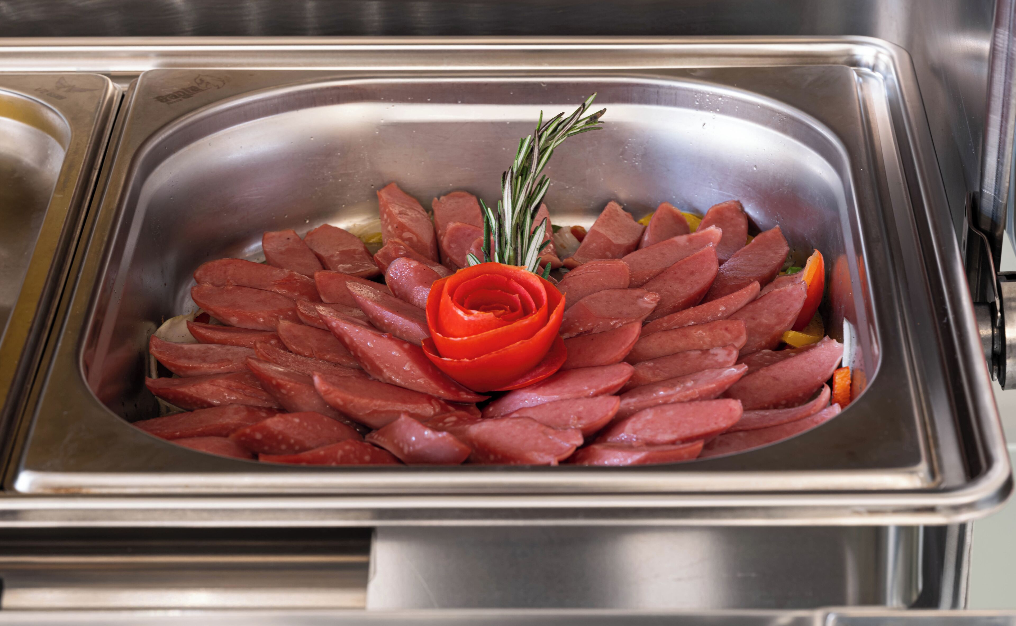 A stainless steel buffet sink with sliced sausages and a decorative red rose.