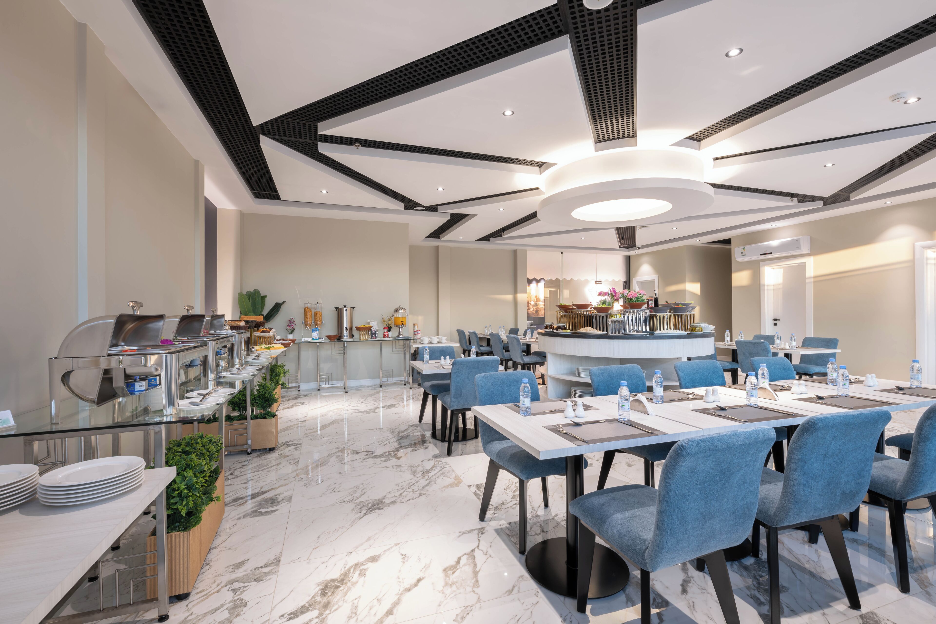 Un comedor moderno de hotel con suelo de mármol, sillas tapizadas en azul y una barra central.