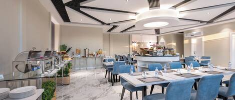 Un comedor moderno de hotel con suelo de mármol, sillas tapizadas en azul y una barra central.