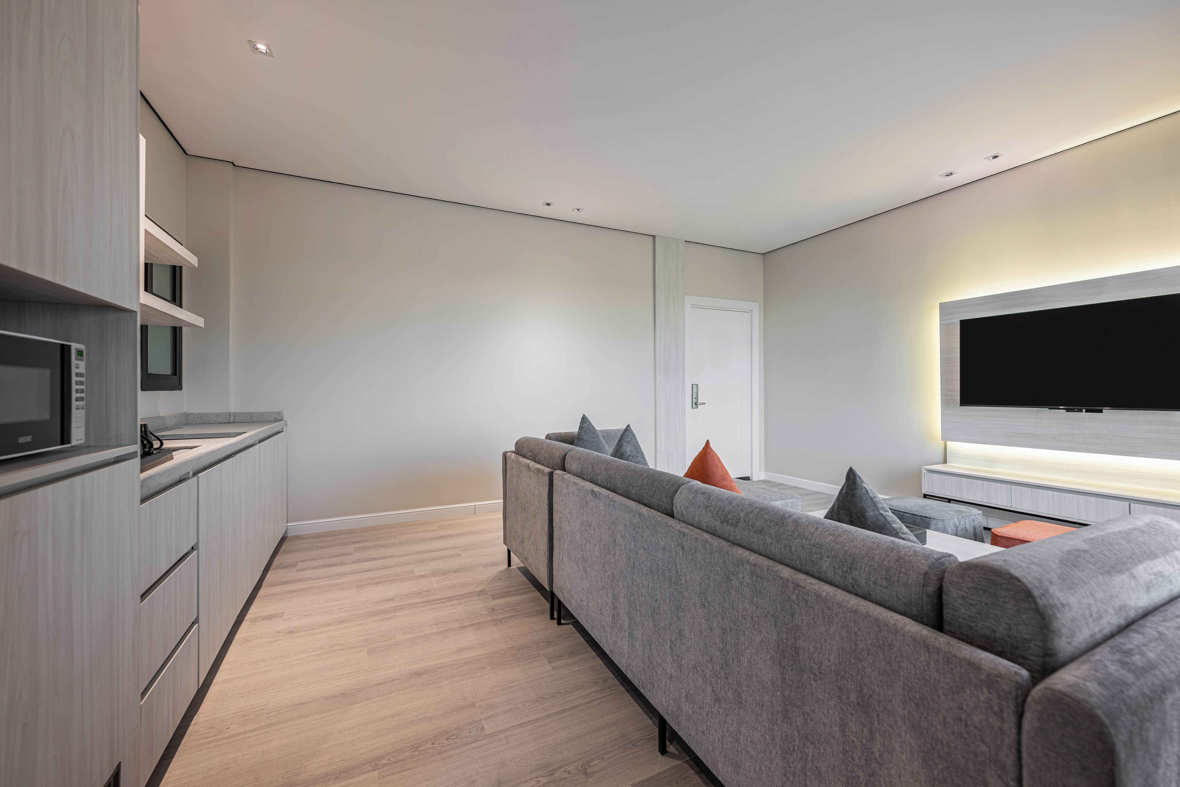 A modern living room with a grey sofa, a flat-screen TV, and a kitchen area with a microwave.