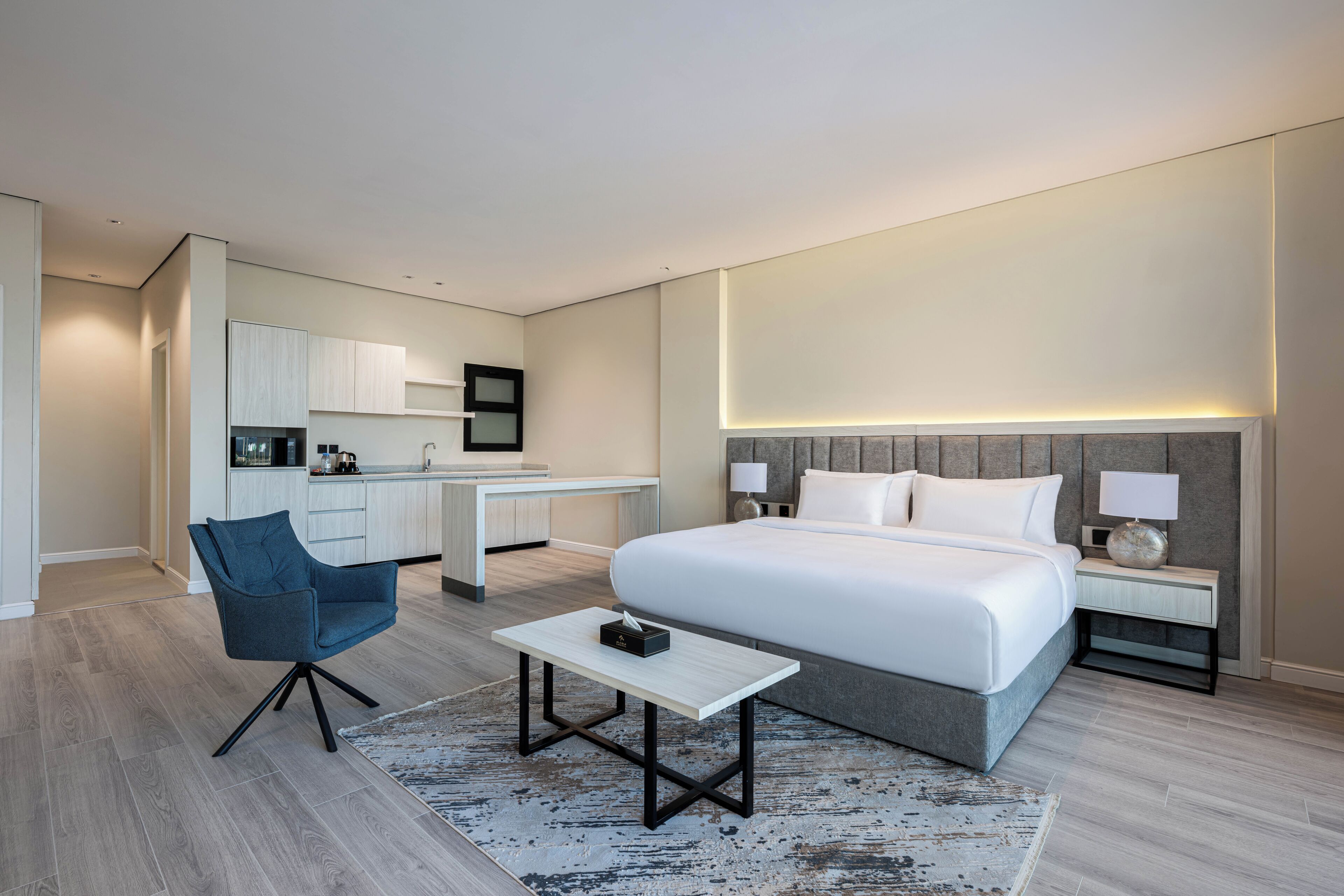 A modern hotel room with a large bed, a desk, a chair, and a small table.