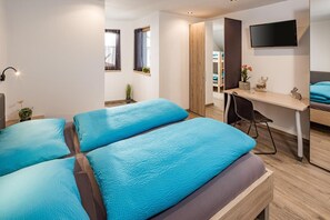 Une chambre d’hôtel moderne équipée de deux lits, d’un bureau, d’une chaise, d’une télévision et d’une fenêtre avec des rideaux.