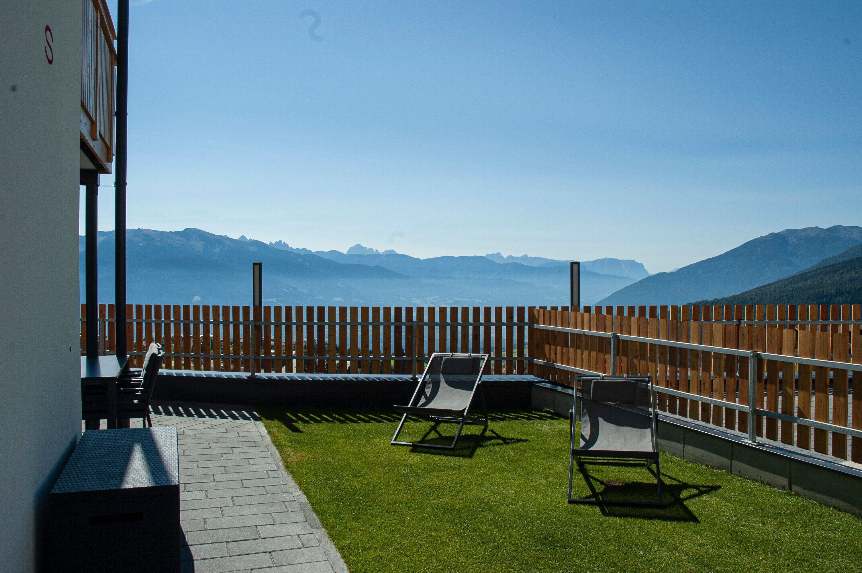 Un balcon avec vue sur les montagnes, une clôture en bois et deux fauteuils de jardin.