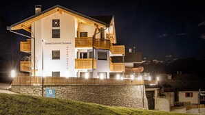 Hotel de vários andares com varandas, um muro de pedra de suporte e uma placa indicando que é um 'Sweet Dolomiti Sonnack'.