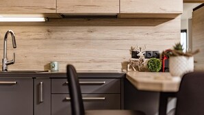 Uma cozinha moderna com painel de madeira, torneira de aço inoxidável e uma cadeira preta.