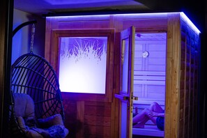 Puisesta laudasta rakennettu sauna, jossa on lasiovi, riipputuoli ja näkyvissä oleva saunapenkki.
