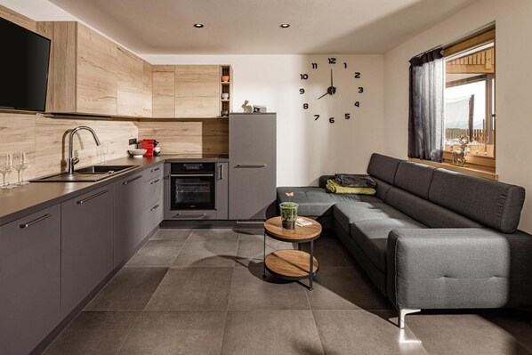 Eine moderne Küche mit Backofen, einem grauen Sofa und einer Wanduhr.