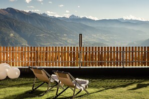 Blick auf eine gebirgige Landschaft von einer Holzdielen-Terrasse mit zwei Liegestühlen und weißen Ballons.