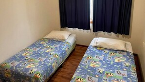 A room with two single beds, each with a blue bedspread featuring cartoon characters. There is a window with dark curtains, and the walls are plain. - HESPS OF BEDS (South West Rocks)