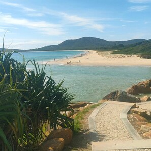 Una playa con aguas cristalinas, una orilla arenosa y un sendero que lleva al agua.