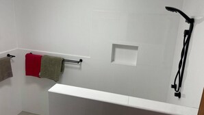 A bathroom with a white bathtub, a towel rack with three towels, and a shower head. - HESPS OF BEDS (South West Rocks)