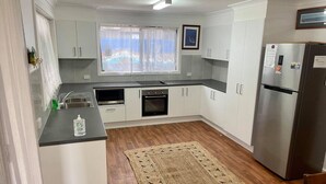 A modern kitchen with white cabinets, a stainless steel refrigerator, and a window with a view. - HESPS OF BEDS (South West Rocks)