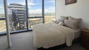 A bedroom with a large window, a bed with a textured blanket, and a wall-mounted sign. - Cosy 2 Bedroom Apartment With Pool, gym and Sauna (Melbourne)