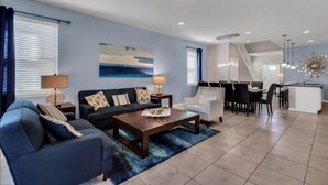 A modern living room with a sofa, coffee table, and dining area. - Spacious 7 BR Villa with Pool, Spa, Themed Rooms (Kissimmee)